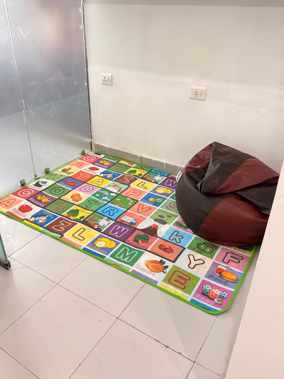 A colourful alphabet-themed play mat and cozy bean bag chair in the sensory play corner at Kiddicove Gurugram.